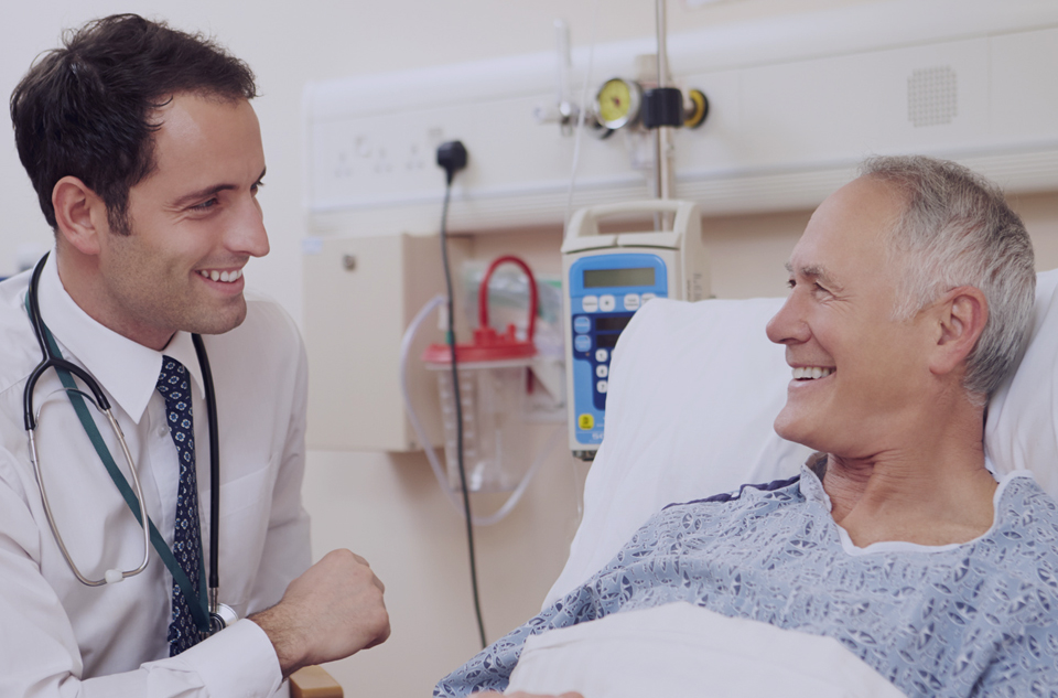 Doctor interacting with a smiling elderly patient in a hospital room.